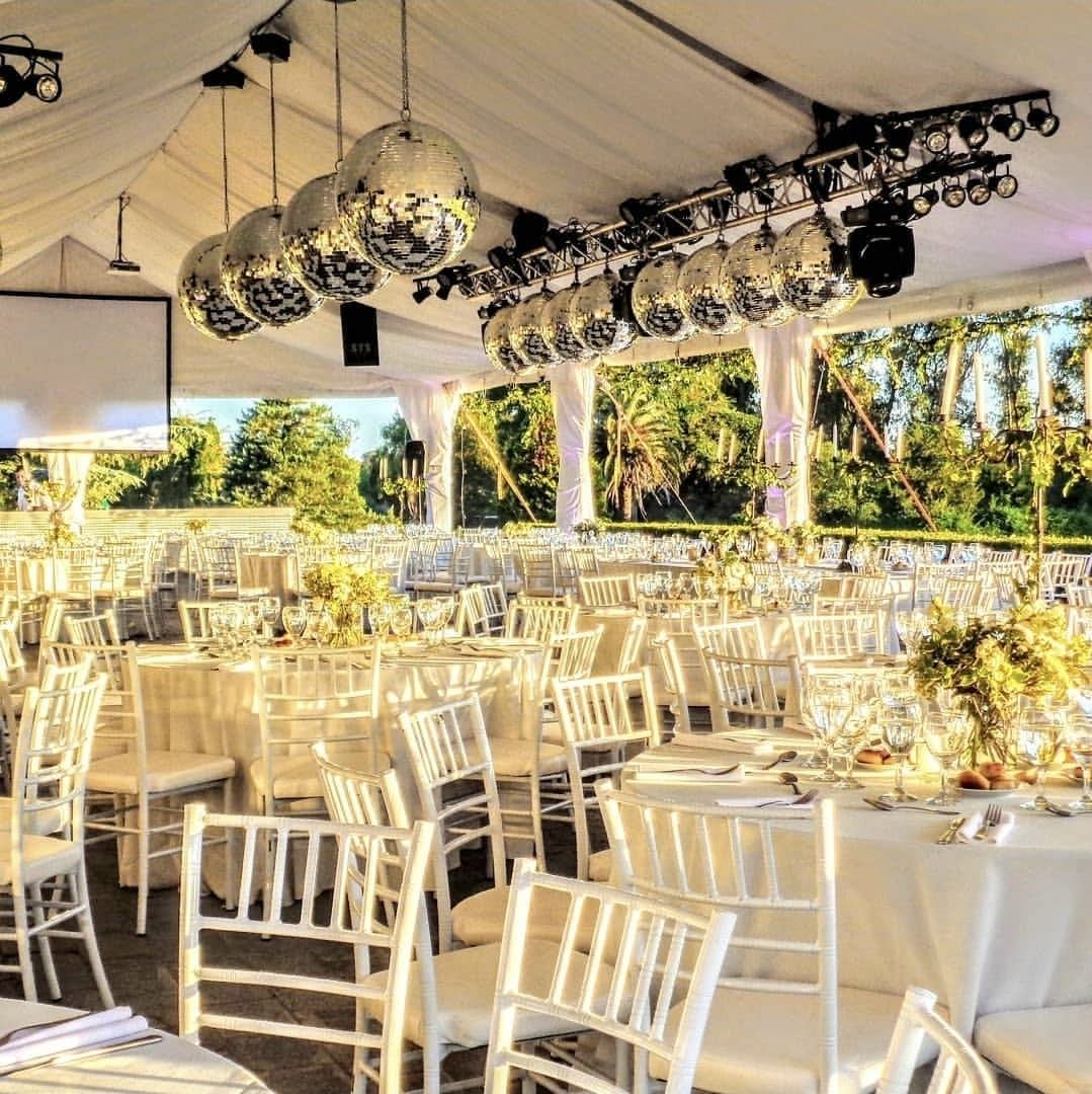 Carpa montada para un evento con mesas vestidas de blanco y bolas de espejos